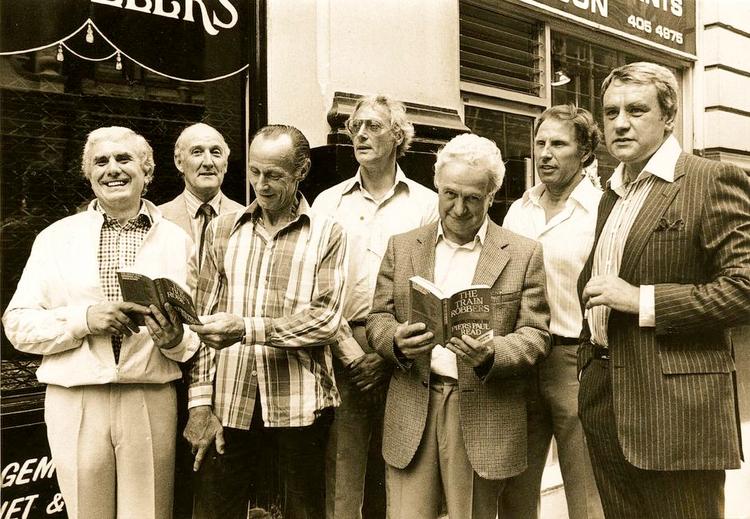 Løsladt. I 1979 samledes syv af bandemedlemmer i anledning af paperbackudgivelsen af en bog om røverne. I midten med briller ses Bruce Reynolds, der døde i februar i år. Øverst et foto fra 1963 af gerningsstedet. 