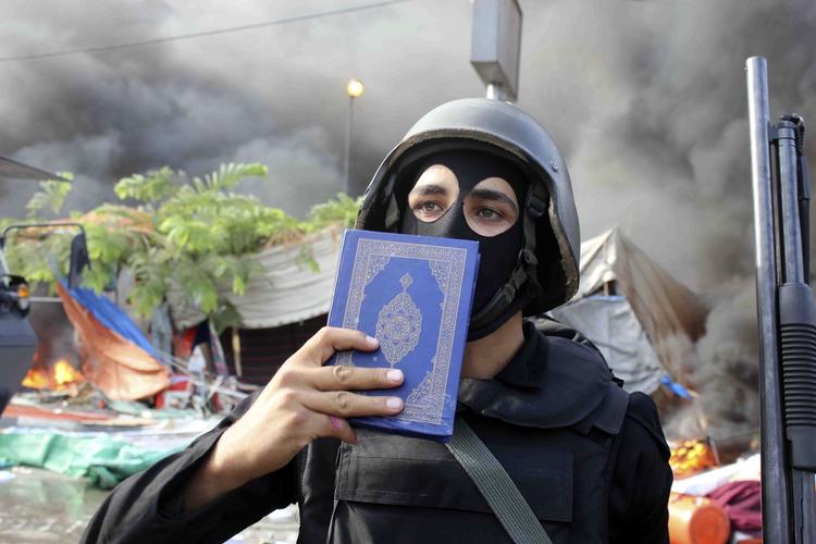 Rydning. Et medlem af af Egyptens sikkerhedsstyrker holder et eksemplar af koranen frem under den voldsomme rydning af demonstrantlejre i Kairo. 