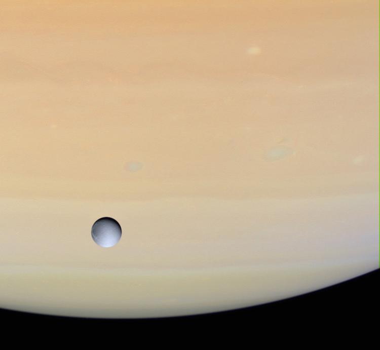 Saturn ledsages af adskillige drabanter (måner). Den følges på sin færd rundt om Solen af over 60 måner. Her er det Dione, der er fotograferet svævende over gasplanetens overflade af Cassini-sonden. 