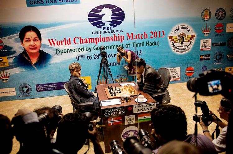 Krydsild. Magnus Carlsen studerer forsamlingen af fotografer på den anden side af glasset, mens matchens officielle fotograf i baggrunden har fået eksklusiv adgang til den boks, hvor partierne spilles. Efter de første ti minutter af hvert parti ryger fotograferne ud. 