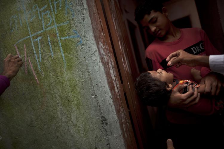 POLIOBEKÆMPELSE. Mens familiens mindste får sin vaccine sætter en sundhedsarbejder et mærke på huset for at vise, at poliobekæmpelseskampagnens mandskab har besøgt hjemmet. 