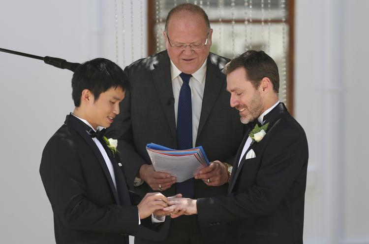 Ægtefolk. Ceremonimester Rodger Munson (midten) ser til mens Chris Teoh (tv.) sætter vielsesringen på Ivan Hinton's finger  foran Old Parliament House i den australske hovedstad  Canberra. 
