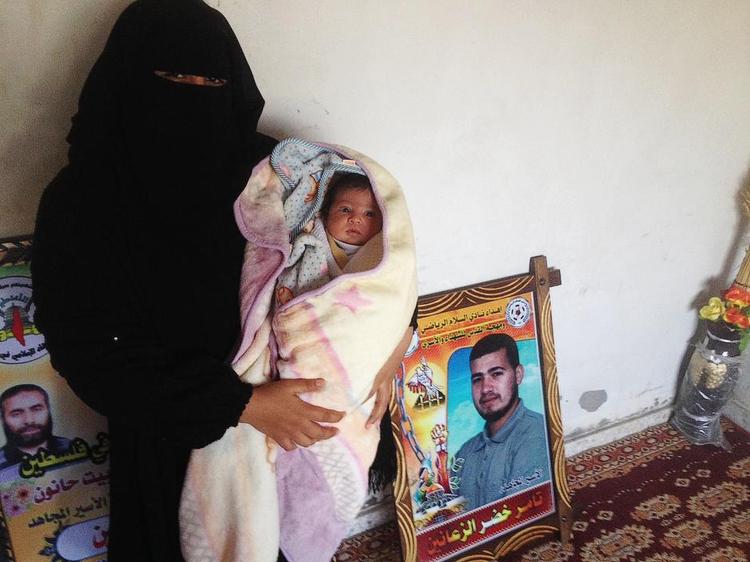 Opfindsom. Mor Hanan med sønnen al-Hassan på armen og fængslede far Tamer på billedet i baggrunden. For snart 11 måneder siden fik Tamer smuglet sin sæd ud fra fængslet. 