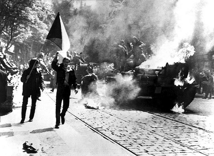 Demonstranter med et tjekkisk flag går forbi en brændende kampvogn på en gade i Prag. 