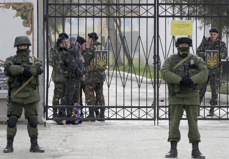 BELEJRING. Russiske soldater har slået ring om en ukrainsk kaserne. Bag hegnet står indespærrede ukrainske militærfolk, en af dem med et barn i armen. 