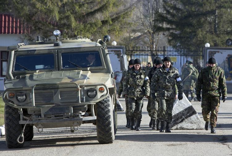 Konflikt. Ukrainske soldater har hvide armbånd på ærmene, mens de marcherer forbi et russisk militærkøretøj uden for en base på Krim 