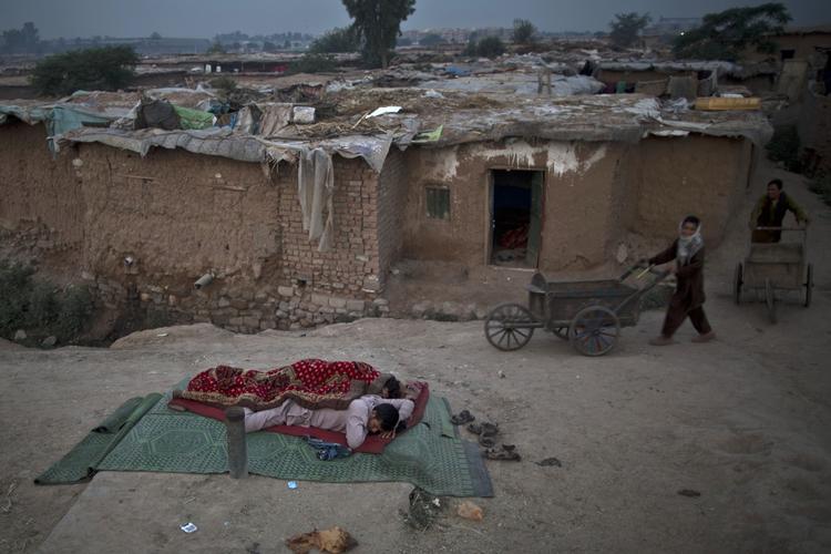 Til højre skubber unge pakistanske mænd deres grøntsagsvogne på vej mod et marked. De kommer forbi to pakistanske mænd, som sover på jorden. Mændene er flygtet med deres familier på grund af kampe mellem Taliban og militæret. 