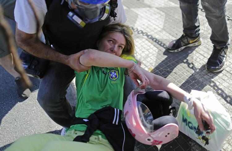 En pressefotograf hjælper en fodboldfan, der er kommet tilskade efter at være kommet i klemme mellem politi og demonstranter foran stadion i San Paulo. 