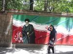 Spænd. Lederen af Irans islamiske revolution i 1979, ayatollah Khomeini, skuer fra muren ved USA's tidligere ambassade i Teheran, mens en moderne ung kvinde passerer forbi med synligt hår og tætsiddende tøj. Iran er midt i en opbrudstid, hvor landet leder efter en balance imellem benhårde ideologer og reformister. 
