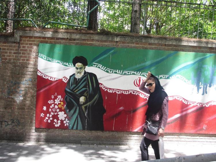 Spænd. Lederen af Irans islamiske revolution i 1979, ayatollah Khomeini, skuer fra muren ved USA's tidligere ambassade i Teheran, mens en moderne ung kvinde passerer forbi med synligt hår og tætsiddende tøj. Iran er midt i en opbrudstid, hvor landet leder efter en balance imellem benhårde ideologer og reformister. 