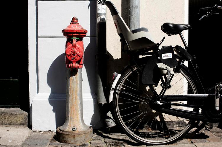 Cykelparkering. Til venstre for nedløbsrøret kan man parkere sin cykel uden konsekvenser. Men på højre side af røret ligger en af Cykelstativets kunder, og her fjerner firmaet dem, så cyklerne ikke fylder foran facaden. 
