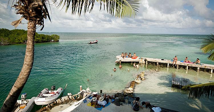 Presset. Badegæster hygger sig ved Caye Caulker i Belize. Strandbyen tiltrækker normalt backpackere med planer om at udforske Belize Barrrier Reef, der er på Unescos verdensarvsliste, men som er også er truet. 