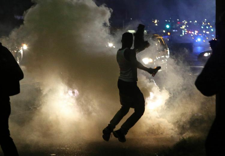 optøjer. Demonstranter løber væk fra politiets tåregas i Ferguson i Missouri, USA. Demonstranterne har været på gaden i tusindvis, siden en sort 18-årig teenager i forrige uge blev skudt af en hvid betjent. 