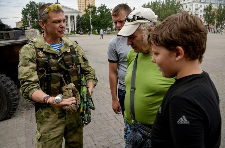Militært. En pro-russisk oprører patruljerer i storbyen Donetsk. Han har tid til at vise en granat frem for indbyggere. 
