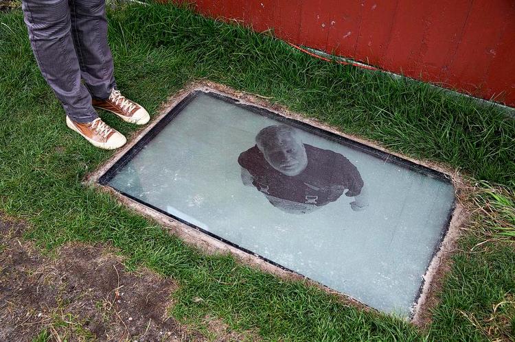 Overraskelse. Katja Bjørn arbejder ofte med videoer, der bliver vist på overraskende vis. Når man træder hen foran det lille skurhus, hvor hendes værk gemmer sig, opdager man noget, der ligner et ovenlysvindue i jorden. Går man endnu tættere på, kan man se ned i et underjordisk rum, som mennesker træder ind i - og kigger op fra gennem vinduet. 