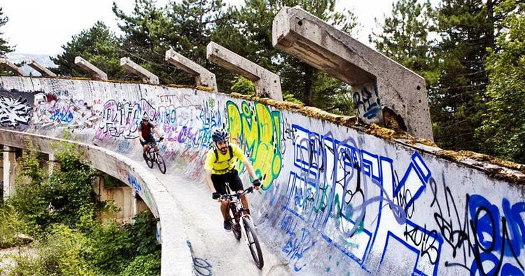summen. Som en bugtende stålorm vrider den 1.300 meter lange bobslædebane sig gennem 13 sving nedad bjerget. Ved Vinter-OL i 1984 var der 30.000 jublende tilskuere, som heppede på bobslædekørerne. I dag hører man kun den summende lyd af mountainbikens nubrede dæk mod den slidte beton. 