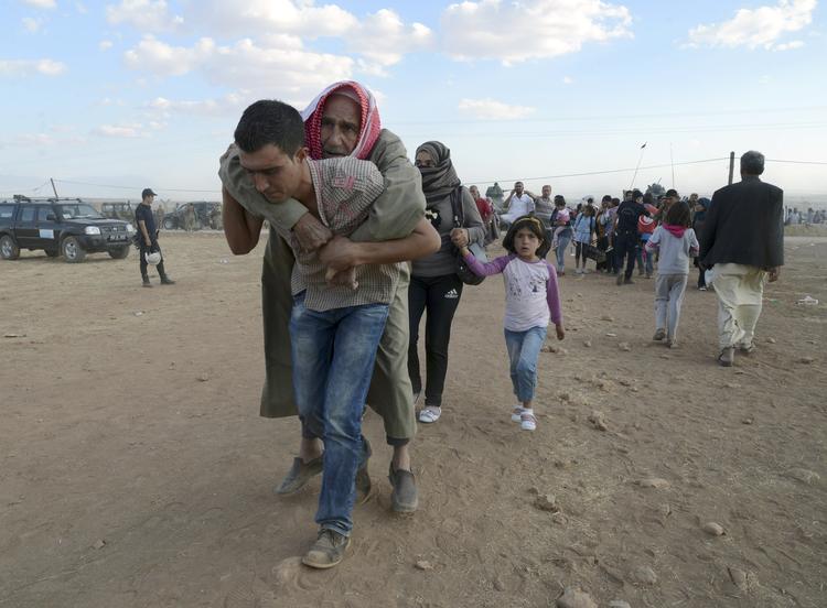 FLUGT. Syrer bærer en ældre kvinde på ryggen op mod grænsen til Tyrkiet under flugten fra Islamisk Stat. 