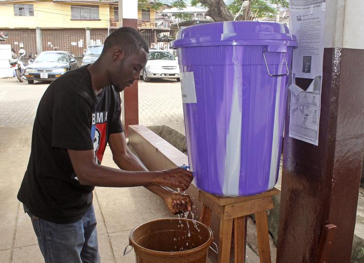 Smitte. En mand vasker sine hænder i desinfektionsvæske uden for et hospital i Freetown i  Sierra Leone. Røde Kors mener,a t der er brug for mere oplysning, hvis sygdommen skal standses. 