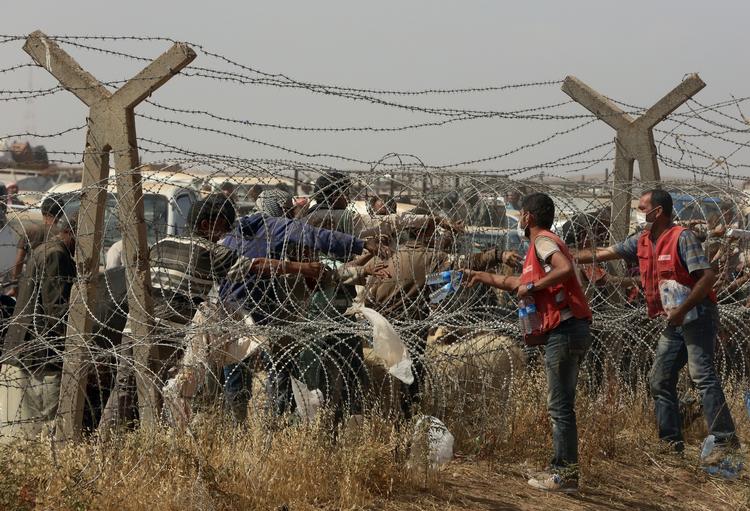 FLYGTNINGEHJÆLP. Tyrkiske hjælpearbejdere rækker vand ind gennem grænsehegnet til Syrien, hvor flygtninge venter på at komme væk fra krigen. 