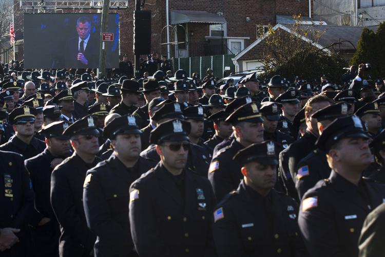 KOLDFRONT. Politibetjente vender ryggen til New Yorks borgmester Bill de Blasio, da han toner frem på storskærm under tale ved myrdet politimands begravelse. 