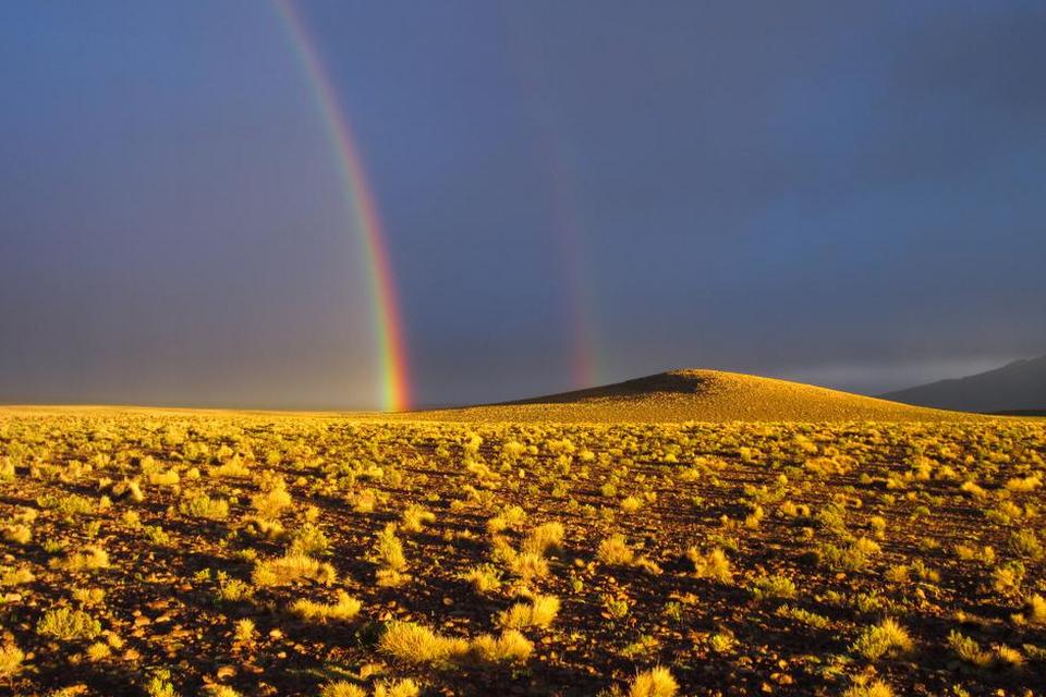 Bolivia. Billedet her er taget under en smuk solnedgang i nationalparken Avaroa i Bolivia, hvori den store saltørken Salar de Uyuni også ligger. »Vi havde kørt længe under tunge skyer med optakt til stormvejr, da solen pludselig brød frem i horisonten og lod sine stråler falde ind over landskabet og gav dette fantastiske farvespil med en meget kraftig dobbeltregnbue«, skriver fotografen. FOTO: Anita Hinz Lyng Sørensen 