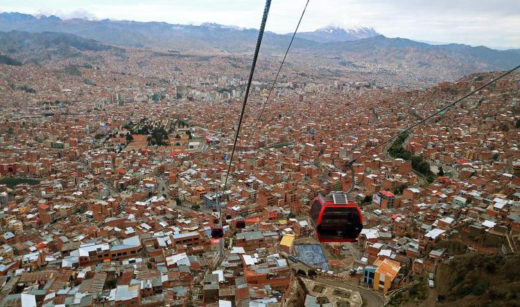 Højt. Den røde svævebane går fra El Alto 4.000 m.o.h. til La Paz' centrum 3.600 m.o.h. Turen er 2,4 km lang og tager 10 minutter. I baggrunden ses det sneklædte bjerg Illimani 6.442 meter højt og vartegn for La Paz. 