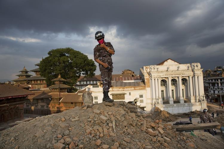 En nepalesisk politimand står på toppen af murbrokker på Basantapur Durbar Square. 
