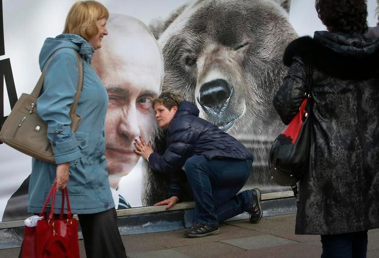Lydhør? En forbipasserende kvinde pjatter ved en plakat med præsident Putin og en bjørn i Sankt Petersborg 1. maj i år. Foto: Dmitry Lovetsky/AP 