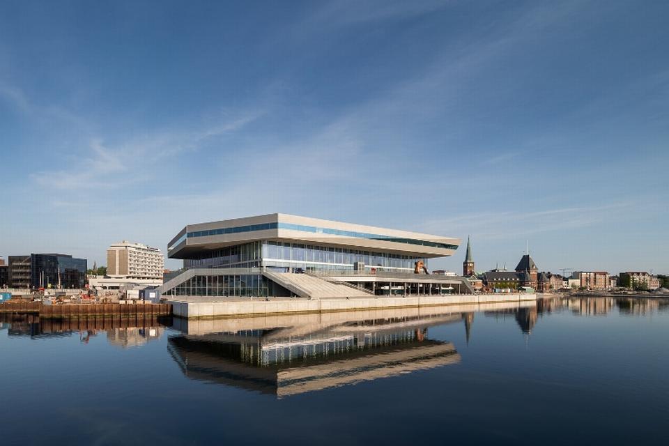 Tagetagen har syv kanter og er skråt afskået mod gaden og mod vandet, hvor trafikken og bølgerne spejler sig i dens vinduesbånd. 