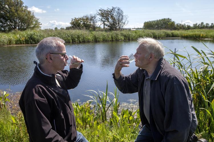 Skål! Byrådsmedlem Asger Møller Madsen (V) (t.v.) og landmand Carsten Søborg (t.h.) skåler i drænvandet fra Carsten Søborgs marker. Målinger fra Aarhus Universitet viser, at det er tre gange renere end kravet til drikkevand. Foto: Søren Schnoor. 
