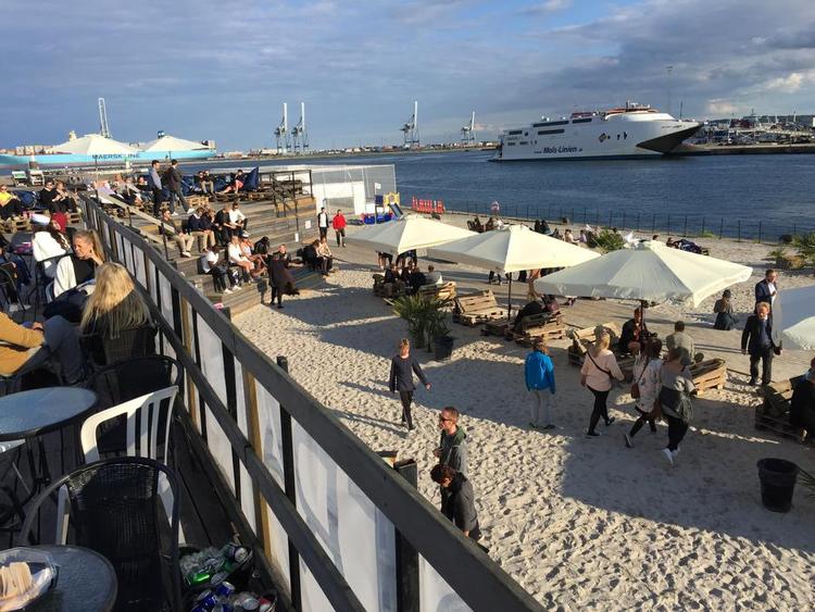 Sol over Aarhus. I Strandbaren i den nye bydel Aarhus Ø kan du hver dag frem til slutningen af sommeren nyde det (forhåbentlig) gode vejr fra en liggestol eller en plads i baren. 
