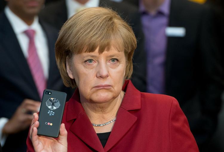Angela Merkel holder en aflytningssikret mobiltelefon op under en IT-messe i 2013. Nu beskyldes hendes egen regering for at have overvåget journalister.  