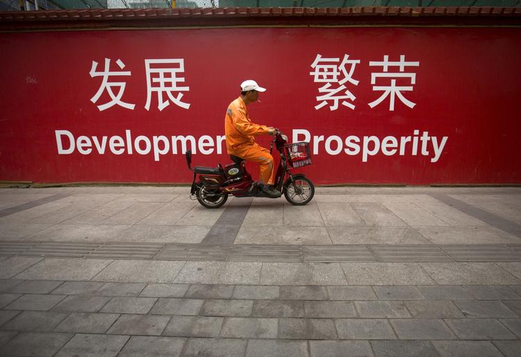 nedgearing. 'Udvikling og velstand' står der på det banner, som denne kineser passerer i det centrale Beijing. Noget kunne tyde på, at målene vil blive opnået lidt langsommere i Kina. 