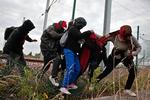 HINDRING. Migranter tiltvinger sig adgang gennem hegnet i den franske kystby Calais, hvorfra de håber at kunne komme til Storbritannien. 