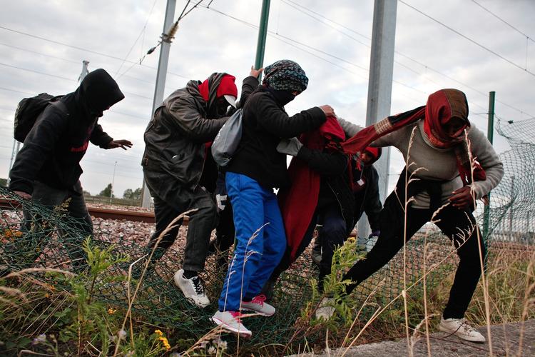 HINDRING. Migranter tiltvinger sig adgang gennem hegnet i den franske kystby Calais, hvorfra de håber at kunne komme til Storbritannien. 