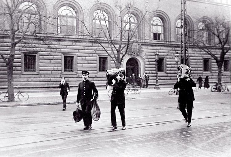 Fremsynet. I romanen 'Brødrene Menthe' foregriber Peter Nansen Landsmandsbankens krak i 1922, hvor staten måtte imødegå de mange tabte millioner ved at øge seddelmængden. Her ses Nationalbankens bude på vej over gaden med penge til Landsmandsbankens tomme kasse 