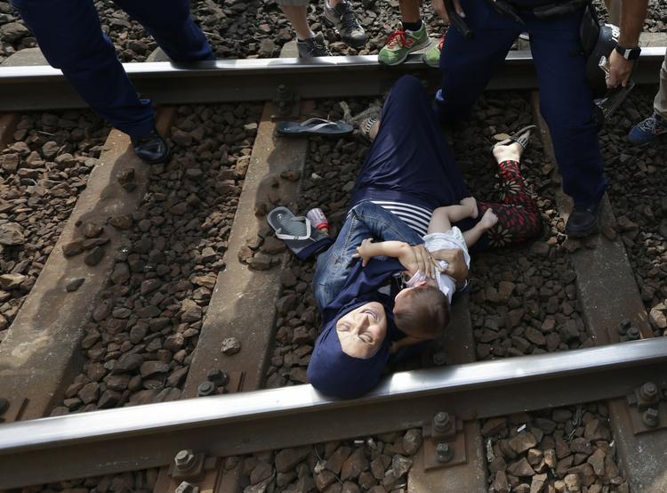 Internationalt. En kvindelig flygtning ligger tilbage på togsporet i byen Bicske med hendes spædbarn. Kort forinden er hendes mand blevet ført væk af bevæbnet politi, fordi familien blokerede togsporet. 