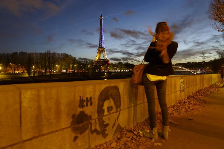 En pige står ved Seinen i Paris og tager et billede af Eiffeltårnet, der efter terrorangrebet i fredags er klædt i franske farver. 