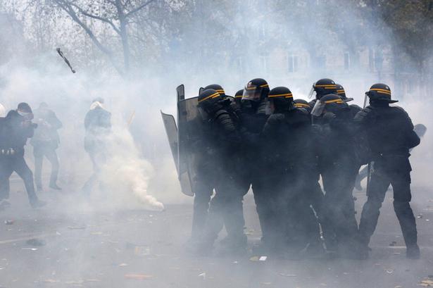 Politi og demonstranter, mange med ansigtet dækket til, støder sammen i udkanten af Place de la République i Paris. Mange demonstranter kaster ting efter politiet, der svarer igen med tåregas. 