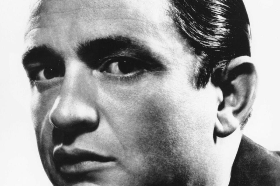 Johnny Cash blev født som J.R. Cash midt i den amerikanske depression 12. februar 1932 i Kingsland, Arkansas. Han voksede op i midten af en søskendeflok på syv. Navnet Johnny Cash fik han først, da han som 18-årig kom i hæren, hvor de ikke accepterede initialer. Selv har han sagt om sit navn: »Sometimes I am two people. Johnny is the nice one. Cash causes all the trouble. They fight«. Som soldat i luftværnet blev Cash udstationeret i Tyskland, og det var her, han købte han sin første guitar og startede et band. Portrættet her er fra 1965, hvor han var 33 år gammel. 