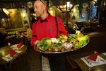 SUR. En tjener bærer et fad smørrebrød ind til gæster på Det Lille Apotek i Indre by. 