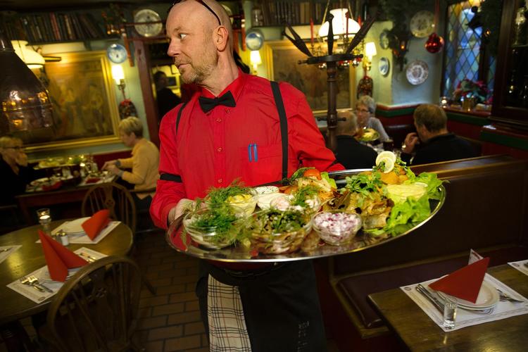 SUR. En tjener bærer et fad smørrebrød ind til gæster på Det Lille Apotek i Indre by. 