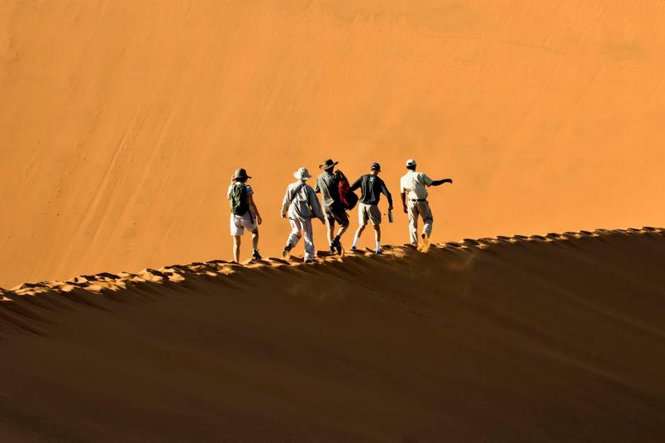 SAND. Lette sko er at foretrække i ørkenen Sosussvlei i det sydvestlige hjørne af Namibia, da du højst sandsynligt ender med at tage dem af, enten for at køle fødderne i sand, eller fordi de fyldes af det. Her balancerer guiden Athanasius og en gruppe turister mod toppen af Big Daddy. Det kan være en strabadserende tur, men også højdepunktet på besøget i Sossusvlei. 