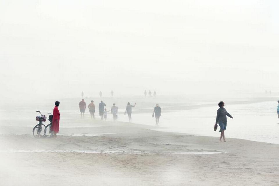 DANMARK. »Skiveren Strand ca. 30 km syd for Skagen på vesterhavssiden. En flot solskinsdag med usædvanligt stille vand, men pludselig sker der noget. Disen strømmer ind over stranden lidt længere nede, så jeg skynder mig derhen. Med ét er det ligesom at være i en helt anden verden. To mennesker er cyklet til stranden for at bade. Kvinden i en rød morgenkåbe står og venter på, at hendes mand skal komme op af vandet og frem af tågen. Længere nede ad stranden forsvinder og dukker mennesker op i tågen på mystisk vis«. Ord og foto: Lars Thomsen 