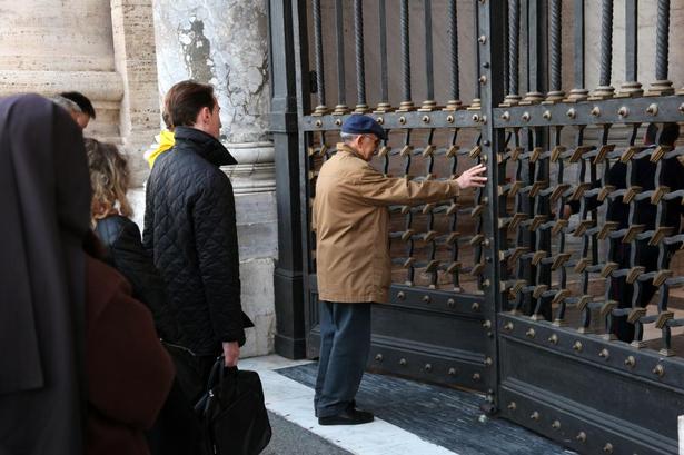 Utålmodig. Klokken er 6.55, og en lille gruppe på et halvt hundrede personer venter foran den store gitterlåge helt oppe foran kirken. En mand kan næsten ikke vente og er ihærdigt med til at skubbe porten op, som bliver åbnet indefra af uniformerede betjente. 