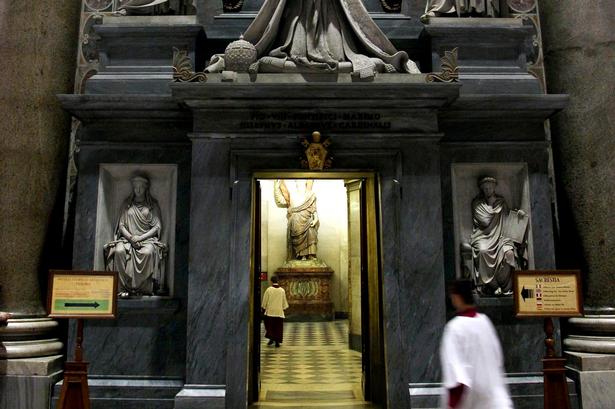 Morgenbønner.  Præster iler ind og ud af den pompøse dør til og fra de tidlige andagter og skriftemål. Portalen, 'Monumento funebre a Papa Pio VIII' ('Pave Pius den 8.s begravelse') er skabt af Pietro Tenerani og udført i 1853-1866. 