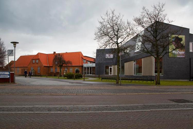 knas. Den lille mellembygning i glas skærer sig ind i taget på hovedbygningen, og den mørke nybygning møder den valmede tagafslutning med en lodret afvisning. 