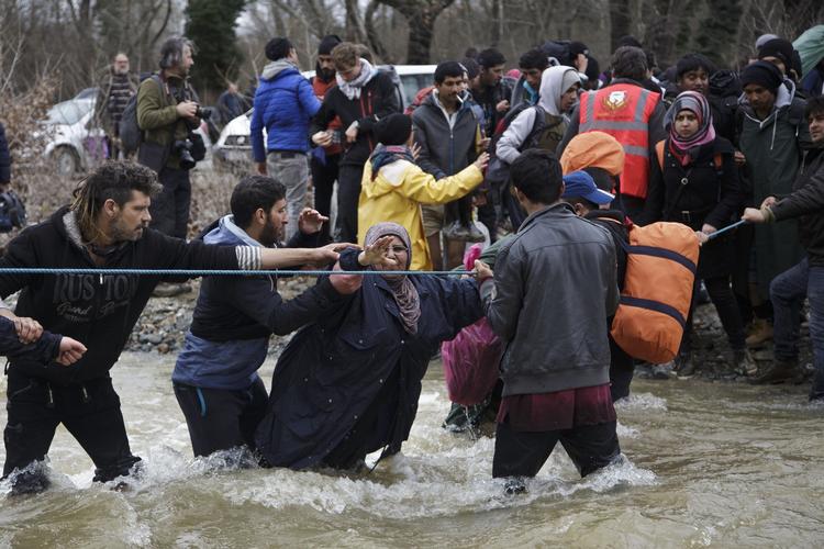MIGRANTRUTE. En aktivist giver en hånd til en kvinde på vej over grænsefloden. 
