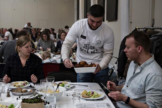 Frivillig. Yasin serverer kyllingefrikadeller for gæsterne og sidder også selv med og spiser og snakker med Daniel Evensen og Nina Jurs. 