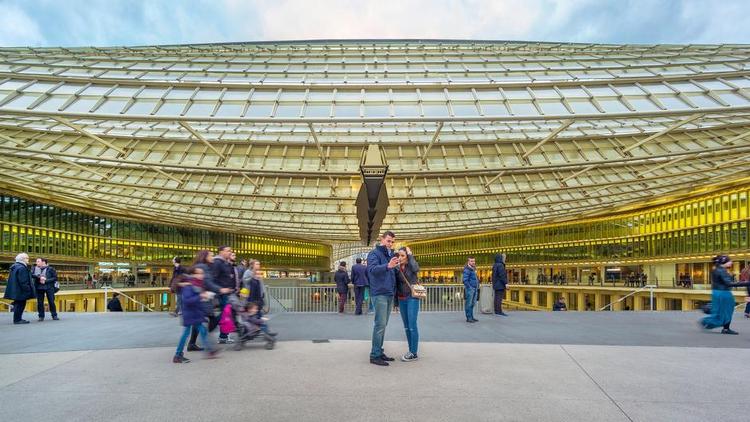 Metalhat. Arkitekten Patrick Berger havde tænkt det som et gigantisk blad, der skulle lægge sig let og beskyttende over de handlende i hullet i jorden, men det fremstår tungt og minder mest om en hængebug. 